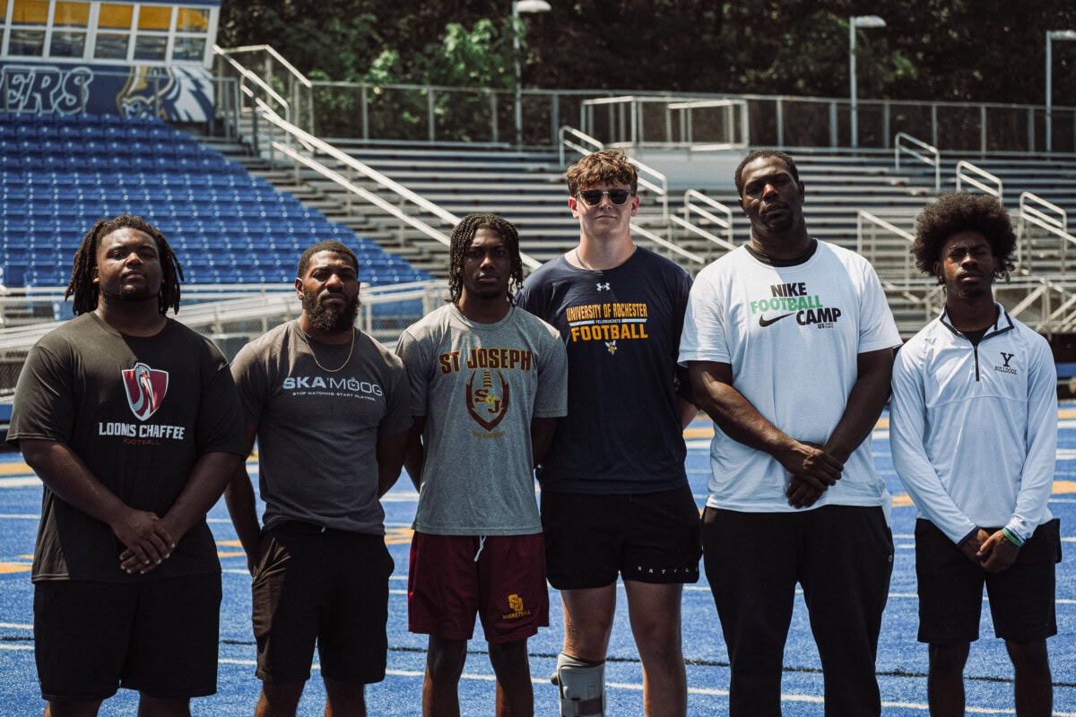 Group photo of coaches and athletes on a football field, promoting football camp.