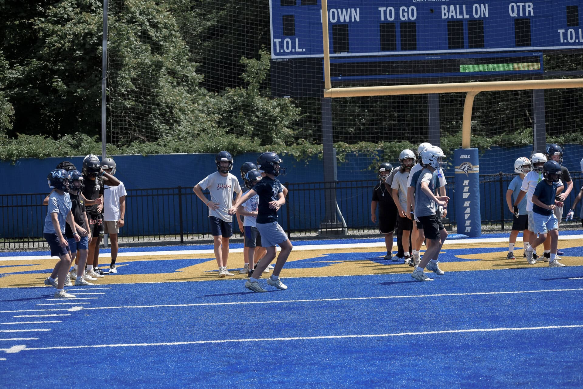 Football team practices on a blue and yellow field under a sunny sky.