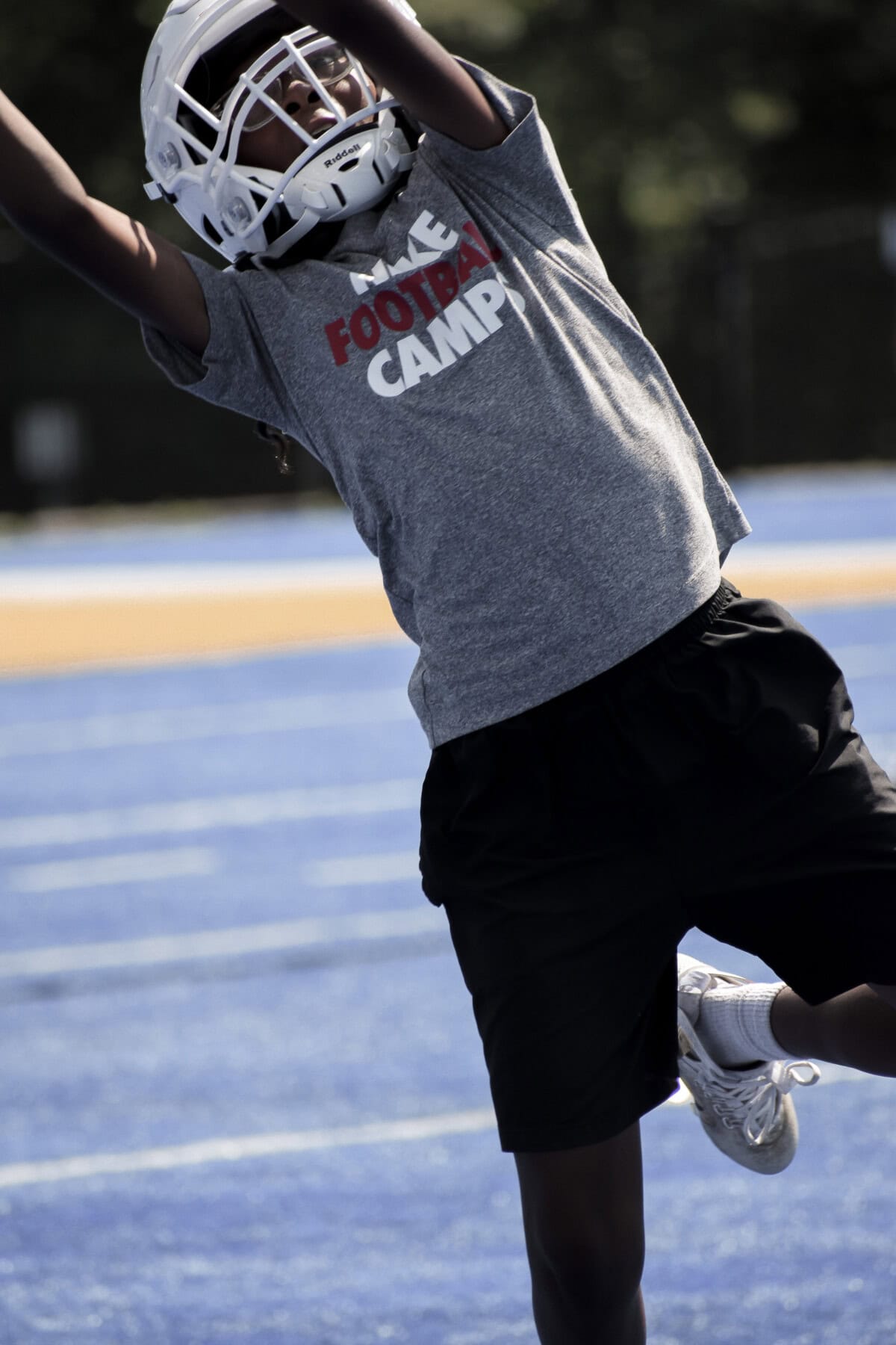 Football player in helmet reaching for a catch at football camp.