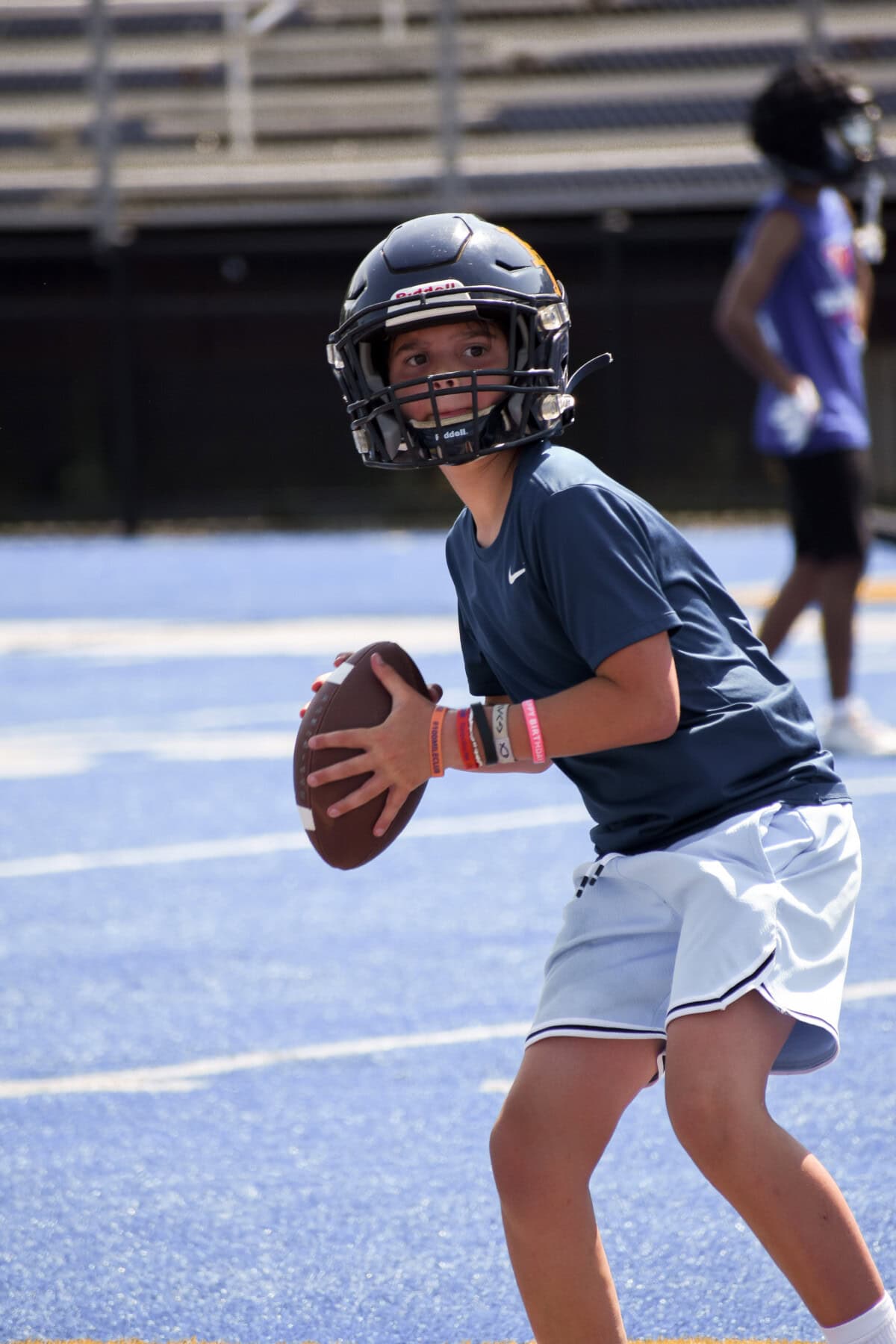 Young football player wearing helmet, preparing to throw the ball on blue turf.