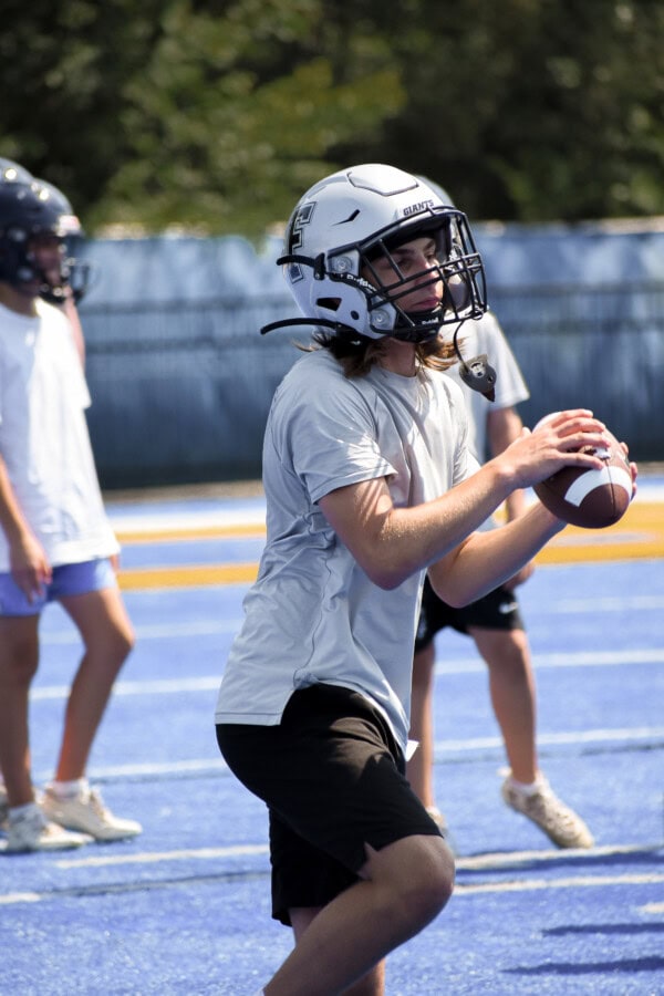Football player in Giants helmet prepares to throw the ball on a blue field.